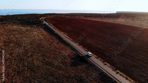 Aerial track shot of lonely van driving on portguese countryside road with beautiful ocean in background. Summer Holiday at algarve,Portugal. photo