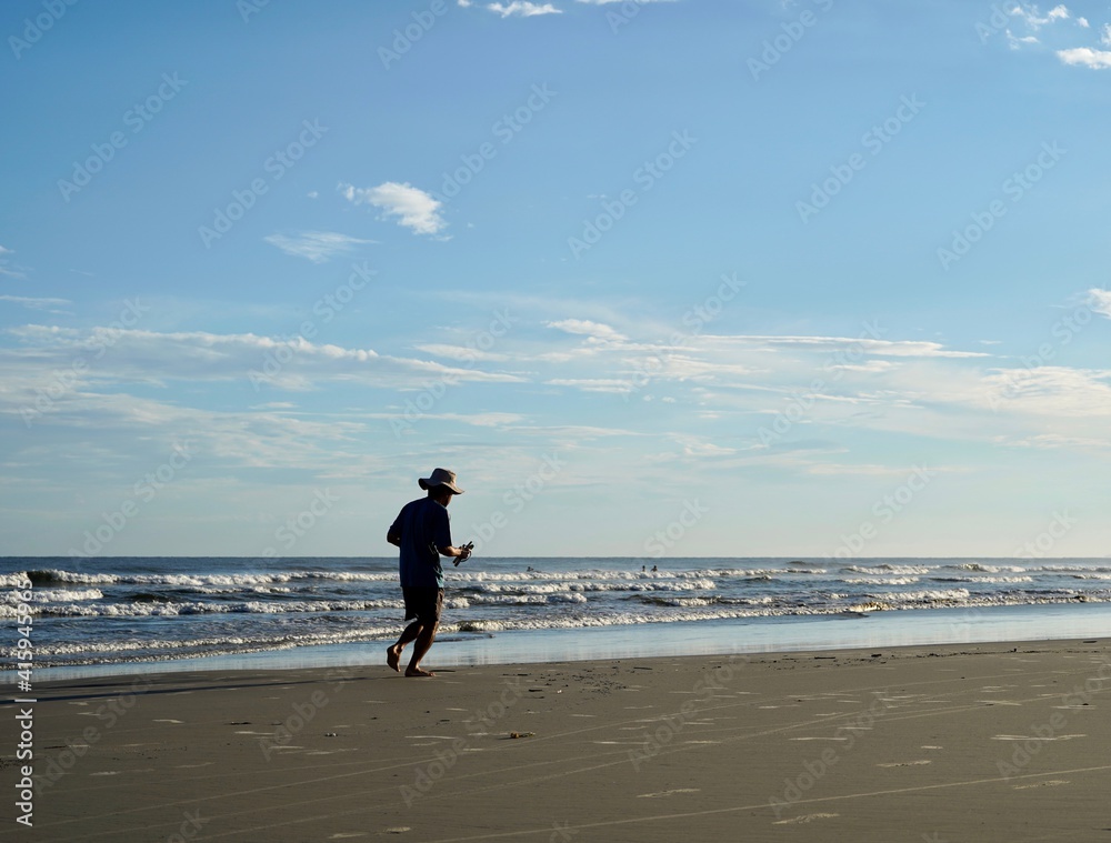 homem usando chapéu e praticando corrida na praia em tarde ensolarada 