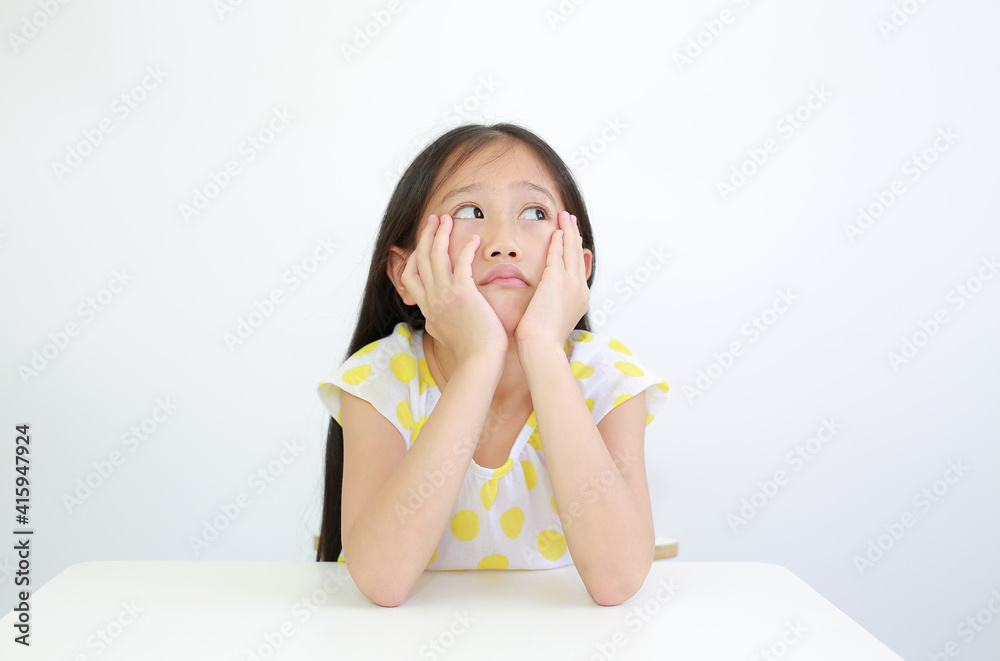 Serious Asian little child girl resting chin on hands with looking up on table over white background Serious Asian little child girl resting chin on hands with looking up on table over white background