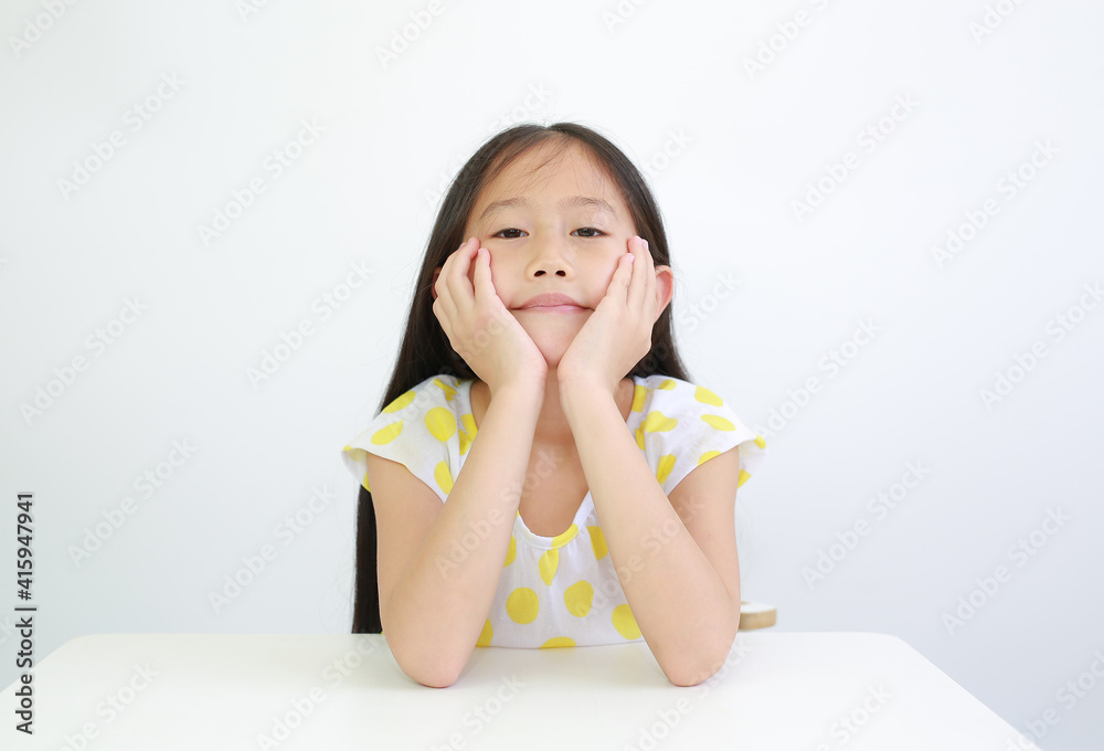 Pretty Asian little child girl resting chin on hands on table over white background Pretty Asian little child girl resting chin on hands on table over white background