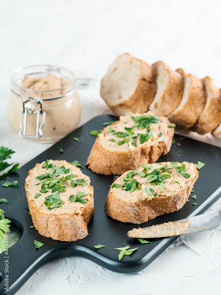 Close up view of slice bread with homemade turkey pate and fresh green parsley on black kutting board over white concrete background, Copy space.