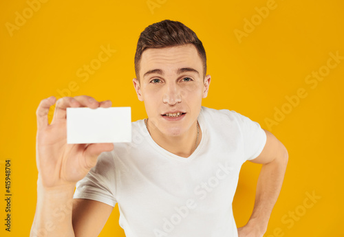 guy in white t-shirt showing business card on yellow background cropped view