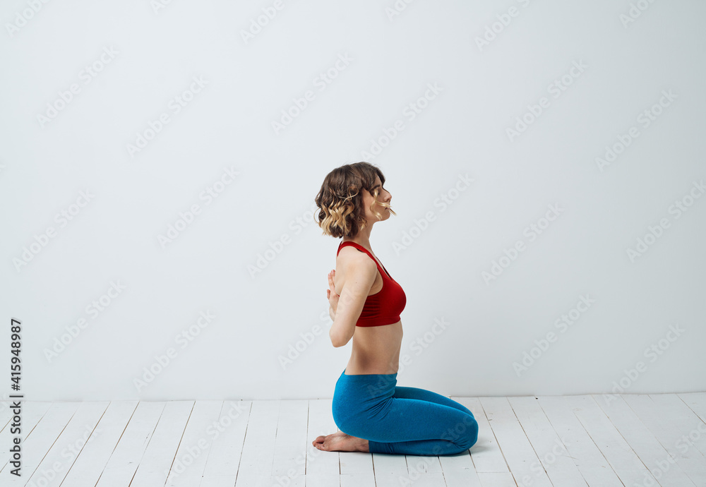 Obraz premium A woman in blue leggings sits on a light floor indoors and holds her hands behind her back