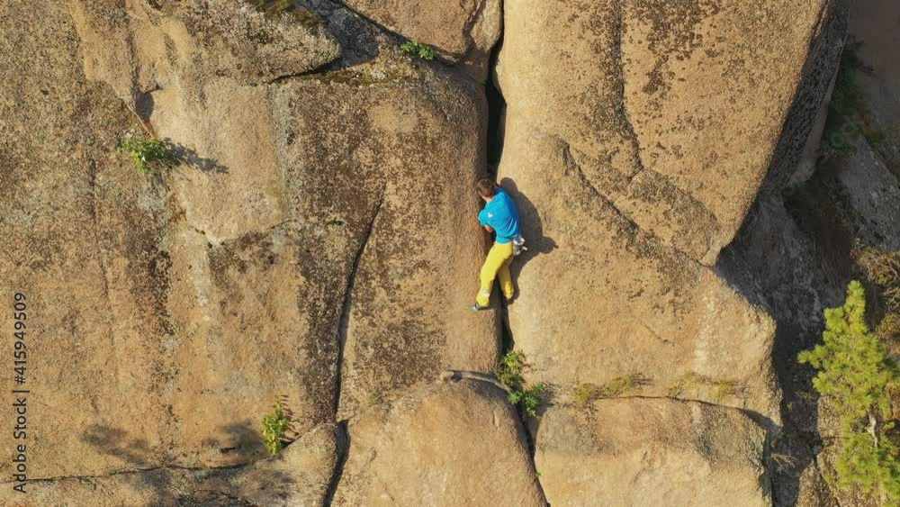 Aerial view of a young man carefully climbs a rock crack Aerial view of a young man carefully climbs a rock crack