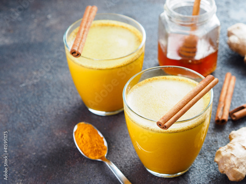 Healthy drink golden turmeric latte in glass.Gold milk with turmeric,ginger root,cinnamon sticks,turmeric powder and honey over black cement background.Detox turmeric tea and ingredients.Copyspace
