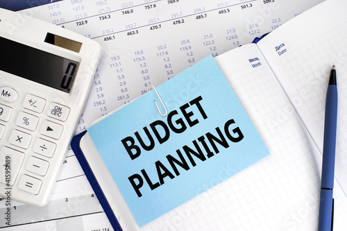 The label budget planning on the blue sheet for notes that is attached to the sheet of notepad. A financial document and a white calculator. Business and financial concept