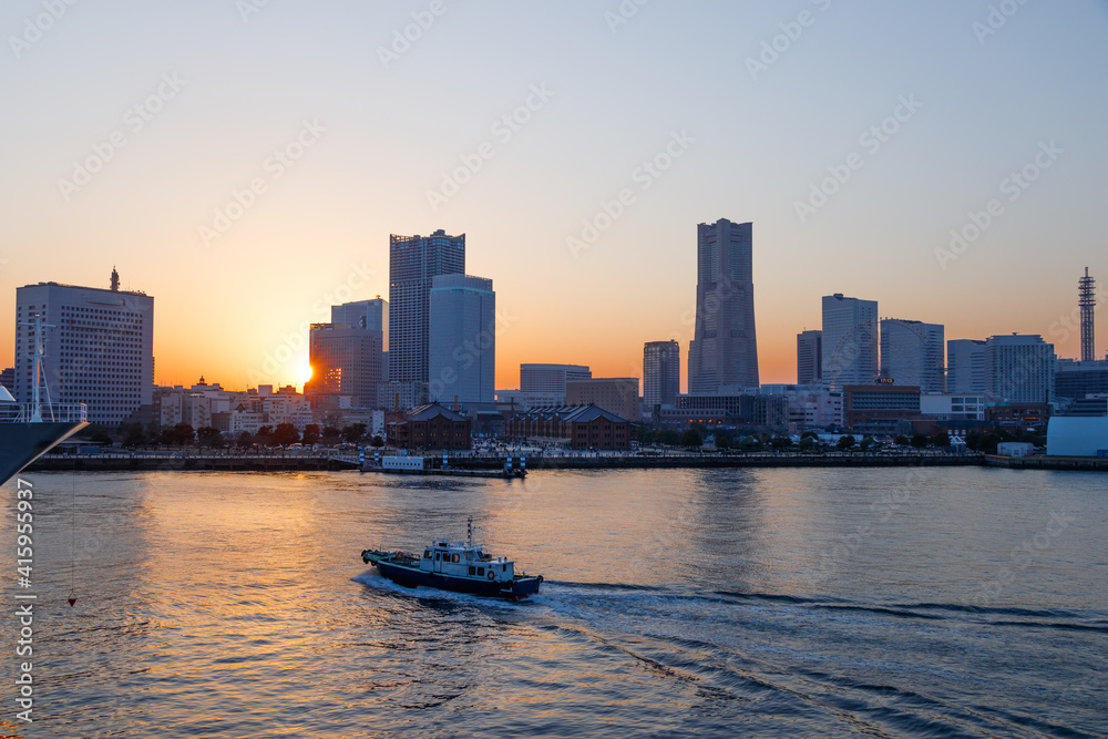 夕陽が沈み始めた横浜みなとみらいのビル群と太陽が反射する横浜港を通過するボート