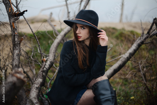 Woman in black hat sitting on fallen tree of dark park