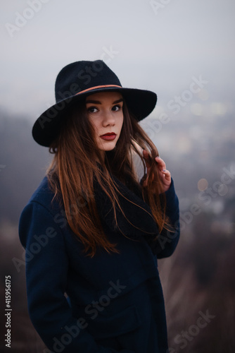 Woman in black hat and coat standing at foggy dark park