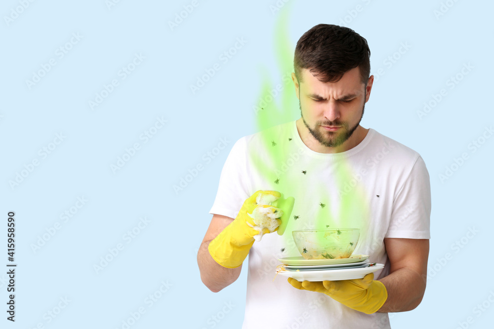 Young man with dirty smelly dishes on color background Young man with dirty smelly dishes on color background