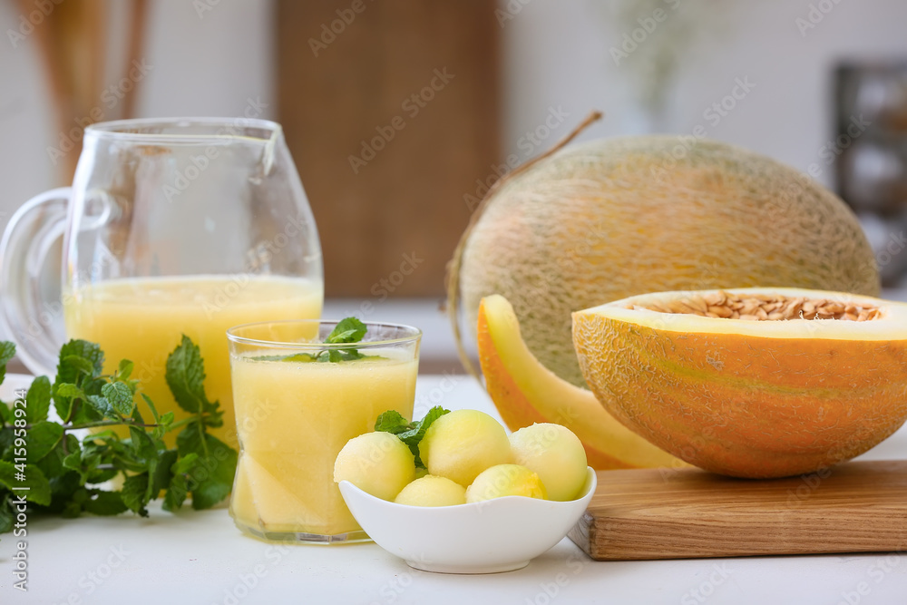Bowl with melon balls and glass of smoothie on table in kitchen