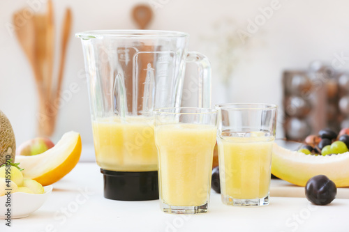 Blender and glasses with melon smoothie on table in kitchen