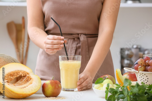 Woman and glass with melon smoothie on table in kitchen