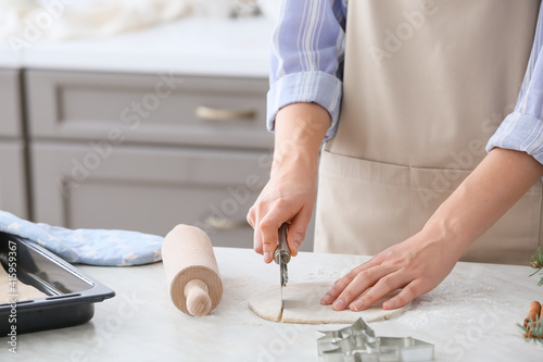 Woman cutting dough on table in kitchen