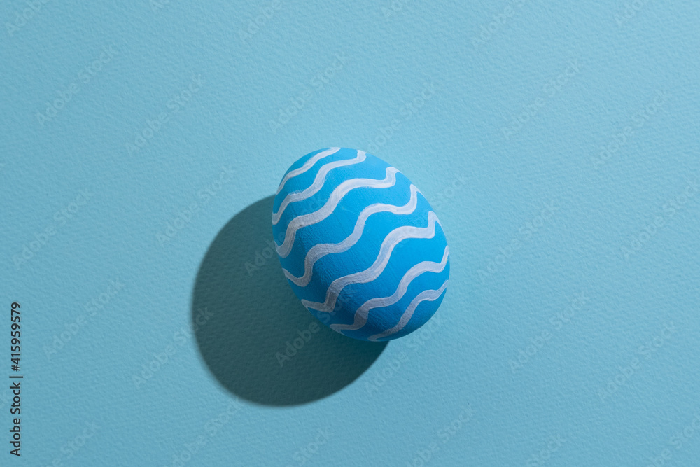 Easter symbol. Festive gift card. Holiday decoration. Abstract background. Blue egg with white zigzag ornament pattern isolated on pastel textured copy space.