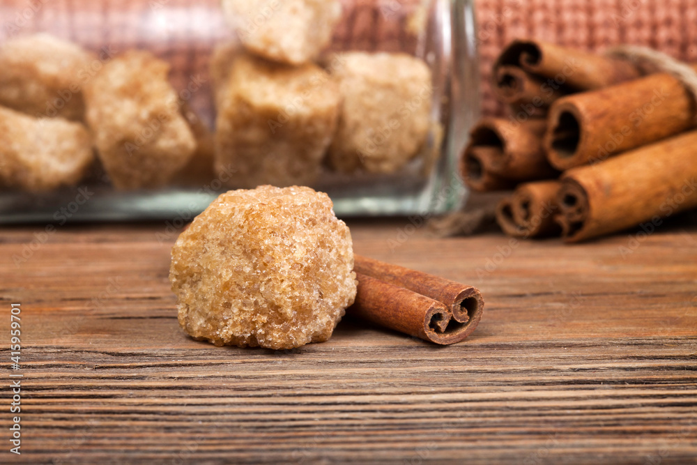 Cinnamon sticks with brown sugar pieces on a wooden background. Macro photography of spices.