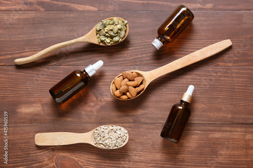 Spoons with different healthy nuts and bottles of oil on wooden background