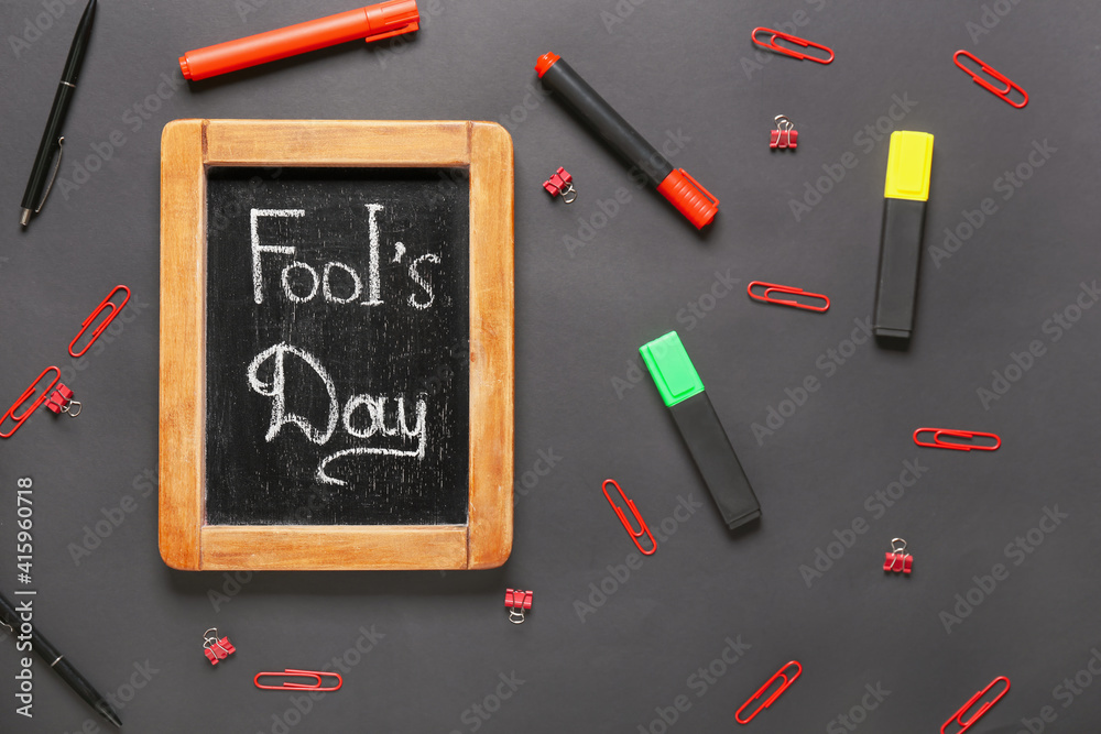 Chalkboard with text FOOL'S DAY and stationery on dark background