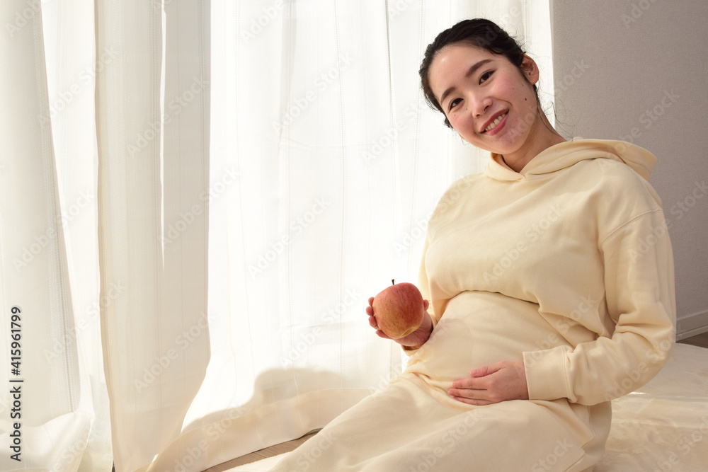 A pregnant woman in her twenties has an apple in front of her big belly. A healthy diet is important during pregnancy. A pregnant woman in her twenties has an apple in front of her big belly. A healthy diet is important during pregnancy.