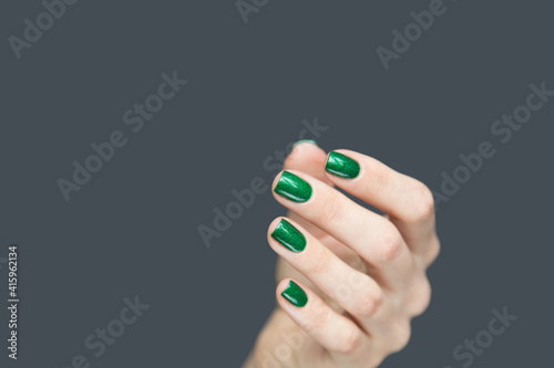 Crop female hand with green manicure. Closeup of gentle female hand with shiny green lacquer on nails isolated on gray background
