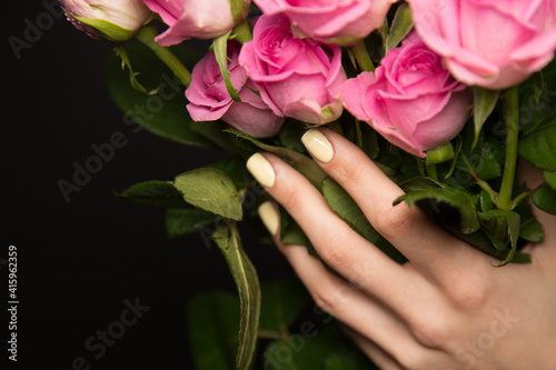 Hand of woman with bunch of roses. Crop female hand with nude beige manicure holding bouquet of pink roses on black background