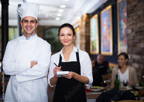 Smiling young waitress with cook chef standing in restaurant photo
