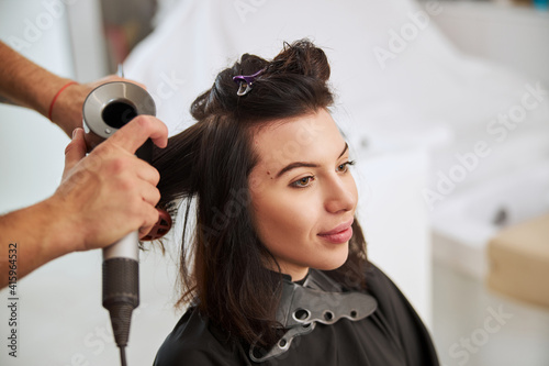 Professional stylist curling female hair with a blowdryer