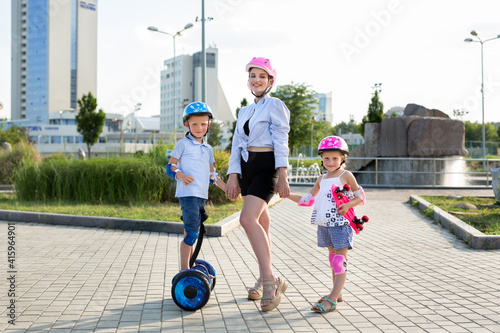 Young mother with her children son and daughter ride a skateboard and gyro scooter in the park.