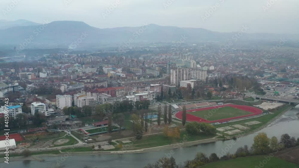 Buildings And Athletic Field On Vast Landscape In Kraljevo, Serbia On A Foggy Day. aerial drone, arc shot Buildings And Athletic Field On Vast Landscape In Kraljevo, Serbia On A Foggy Day. aerial drone, arc shot