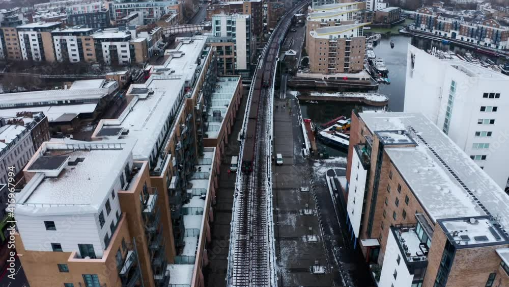 overhead follow drone shot of London DLR train towards Canary wharf from Limehouse in the snow overhead follow drone shot of London DLR train towards Canary wharf from Limehouse in the snow