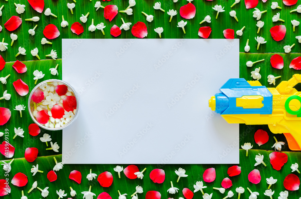 White blank paper with flowers in water bowl and water gun on banana leaf background for Songkran festival. White blank paper with flowers in water bowl and water gun on banana leaf background for Songkran festival.