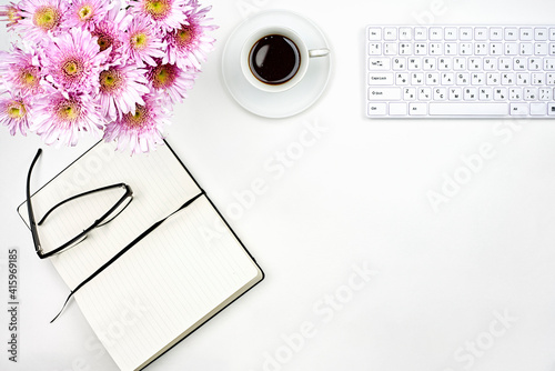 Bright workspace of a businesswoman. Bouquet of fresh spring flowers, notepads and refreshing morning coffee on the working desk