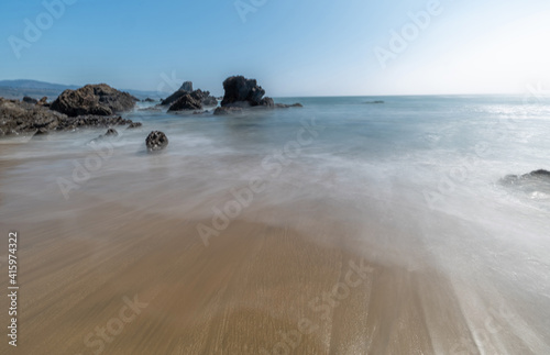 Long exposure water, beautiful seascape of the Pacific coast in California, sandy beach, waves, rocks, sky, sun. Concept, perfect postcard and travel guide.