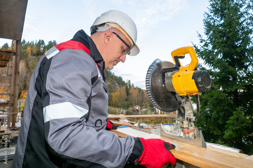 Builder works with a circular saw. Woodworker master. He works in background of nature. Working with a circular saw at a construction site. Career as a woodworker. Preparing wood for construction Builder works with a circular saw. Woodworker master. He works in background of nature. Working with a circular saw at a construction site. Career as a woodworker. Preparing wood for construction