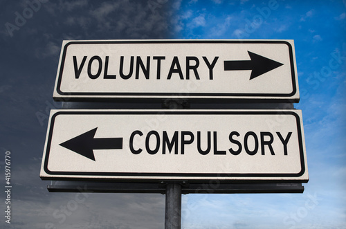 Voluntary versus compulsory road sign with two arrows on blue and grey sky background. White two street sign with arrows on metal pole. Two way road sign with text.