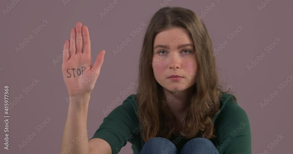 Close-up portrait of Caucasian woman sitting on the floor and raising hand with stop inscription on palm. Stop violence against women. Female rights. Abuse issue