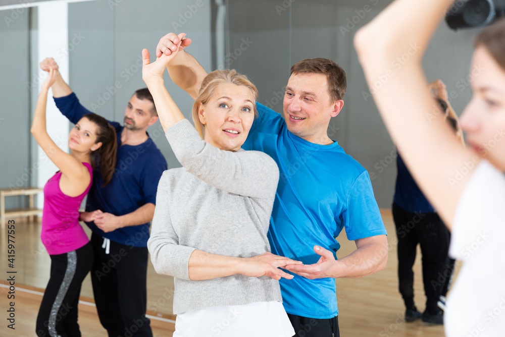 Attractive mature blonde dancing slow ballroom dance in pair during group training in dance hall - obrazy, fototapety, plakaty 