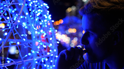 Bokeh view of a stylish young handsome man smoking electronic cigarette and breathing out smoke thru nose in city at night in summer