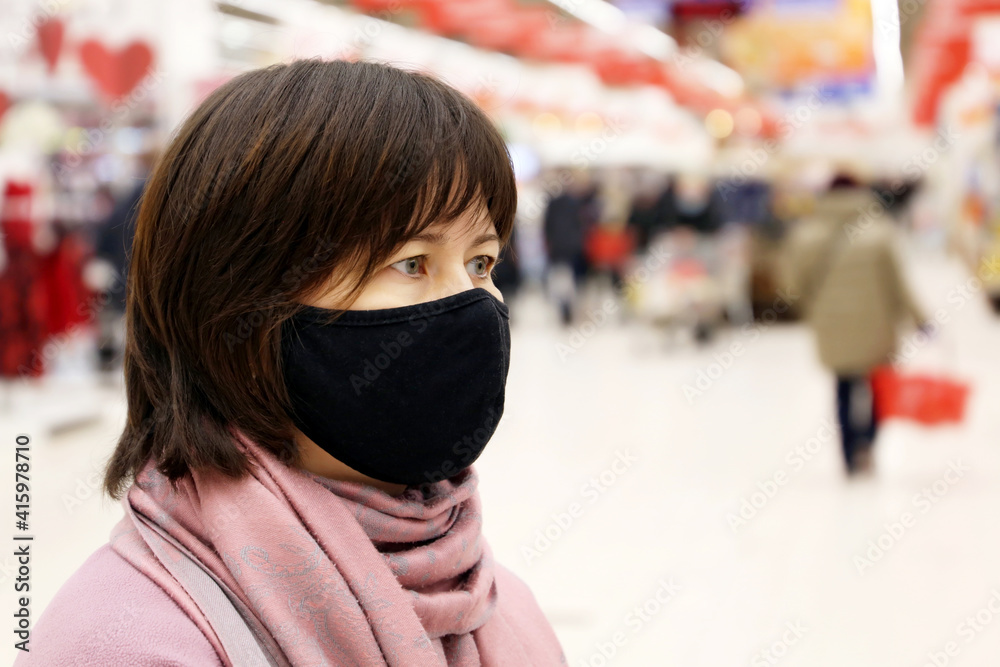 Woman in black protective mask in a shopping mall on people background. Customers in store during quarantine at covid-19 pandemic