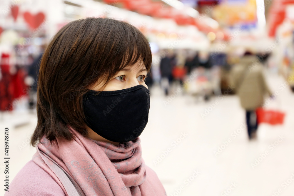 Woman in black protective mask in a shopping mall on people background. Customers in store during quarantine at covid-19 pandemic Woman in black protective mask in a shopping mall on people background. Customers in store during quarantine at covid-19 pandemic