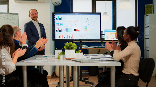 Succesful business man presenting the good evolution of company using digital interactive whiteboard with growth analysis, charts, statistics, data, Diverse people congratulate him clapping