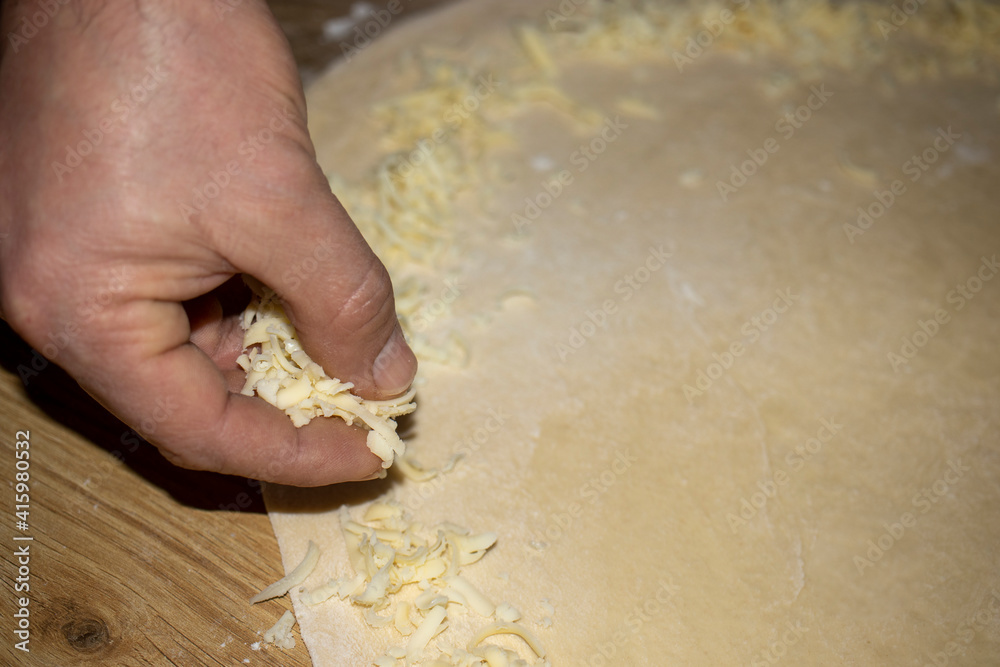 The hands of the cook who put grated cheese on the dough he rolls. The hands of the cook who put grated cheese on the dough he rolls.