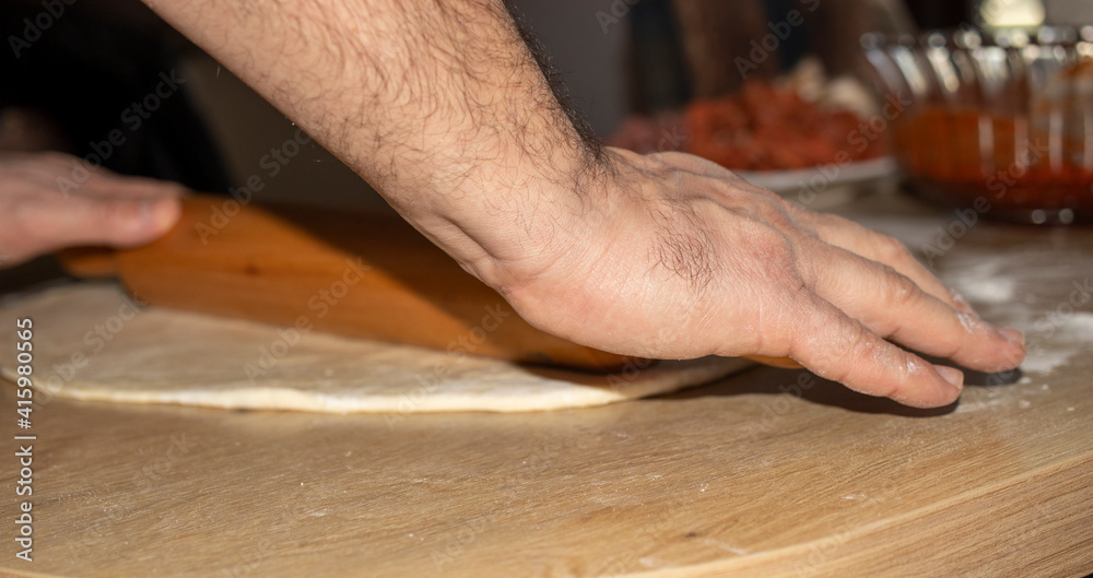 The hands of the cook who put grated cheese on the dough he rolls. The hands of the cook who put grated cheese on the dough he rolls.