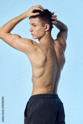 a guy with an athletic figure holds his hands behind his head on a blue background bodybuilder sport