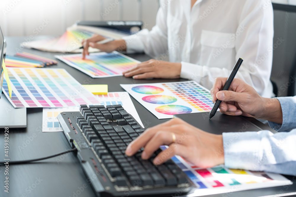 graphic designer team working on web design using color swatches editing artwork using tablet and a stylus at desks In creative office graphic designer team working on web design using color swatches editing artwork using tablet and a stylus at desks In creative office