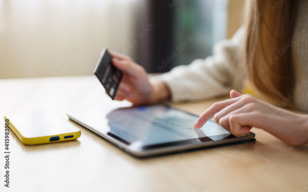 The girl makes a payment with a bank card on the Internet on a tablet. Close-up. Selective focus on the hand near the tablet display. The girl makes a payment with a bank card on the Internet on a tablet. Close-up. Selective focus on the hand near the tablet display.