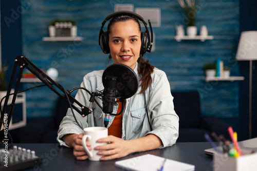 Vlogger messaging her audience while making podcast in home studio for social media. Blogger recording online talk show using headphones, professional microphone looking at camera during broadcast.