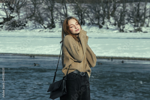Girl in a sweater against the background of a winter landscape. Girl on the river bank. Winter portrait of a girl © Ruzanna