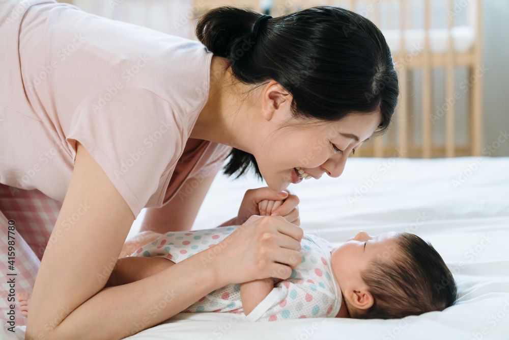 korean new mother with smile leaning toward her baby daughter and holding her hands gently. portrait of mom having strong bonding with baby...mother’s day concept.. korean new mother with smile leaning toward her baby daughter and holding her hands gently. portrait of mom having strong bonding with baby...mother’s day concept..