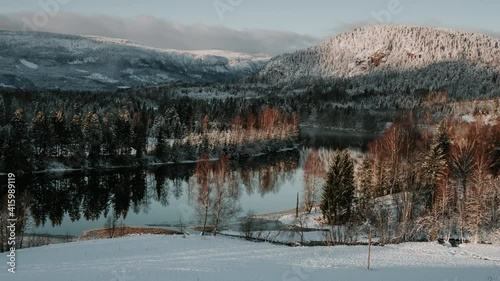 Zooming out time lapse video of beautiful landscape of Southern Norway in winter. Mountains covered in snow, river reflecting trees and clouds  photo